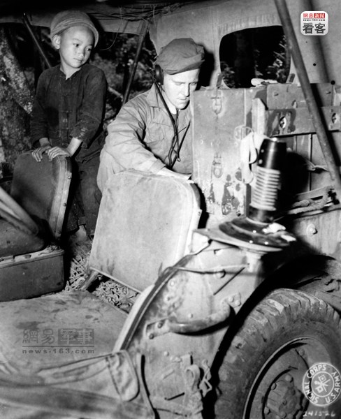 1944年10月12日，在怒江前线的滇缅公路上，美军联络组的无线电员正在操作无线电，引起了一名中国小孩的好奇。摄影师：二等兵　哈特菲尔德。美军通信兵（U