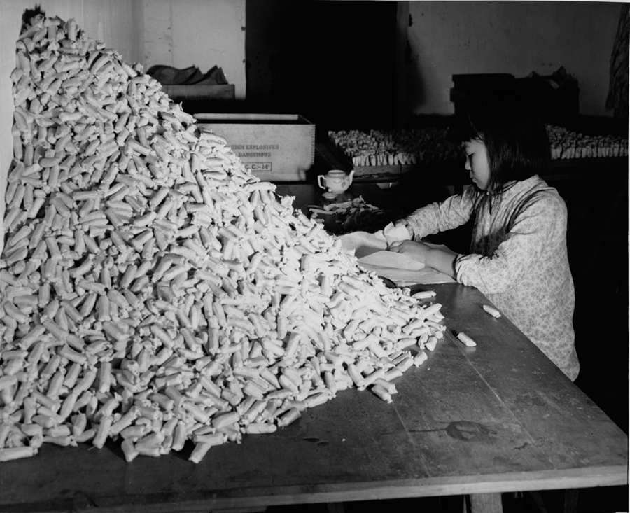 这个小姑娘在一座地下兵工厂里用她灵巧的手指往丝绸袋里填装炸药粉末，用于在工厂另一车间所生产的迫击炮弹内。