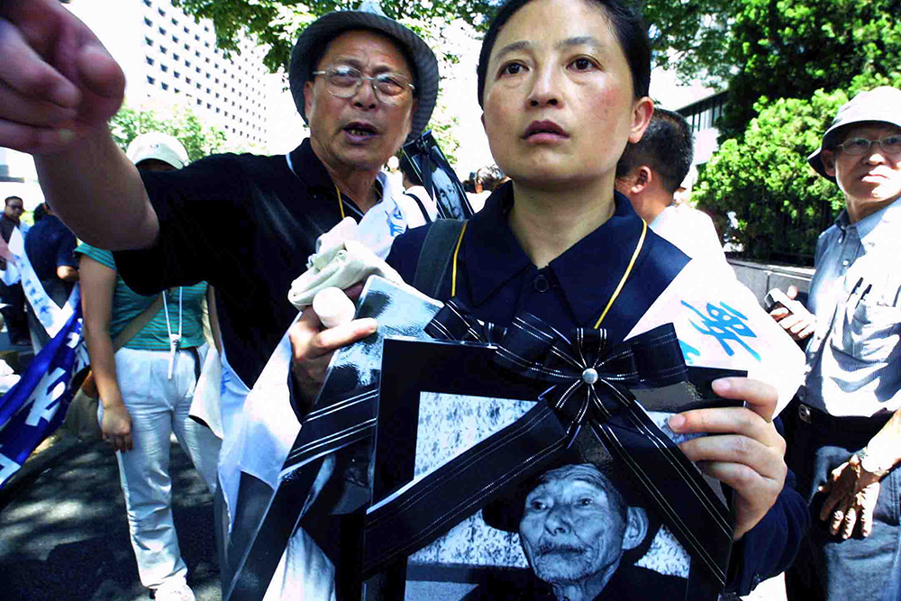 2002年8月27日，日本东京，王选与中国原告手捧已去世的25名原告的遗像，悲愤地抗议东京地方法院一审的不公平判决。    