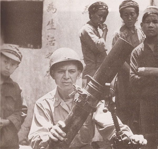 一位美军少校扶着我军缴获的日军迫击炮。这张照片的动人之处，是美军军官身后那位戴着当地独特的头饰、腕戴手镯、正好奇地打量镜头的腾冲女子深邃的眼神。